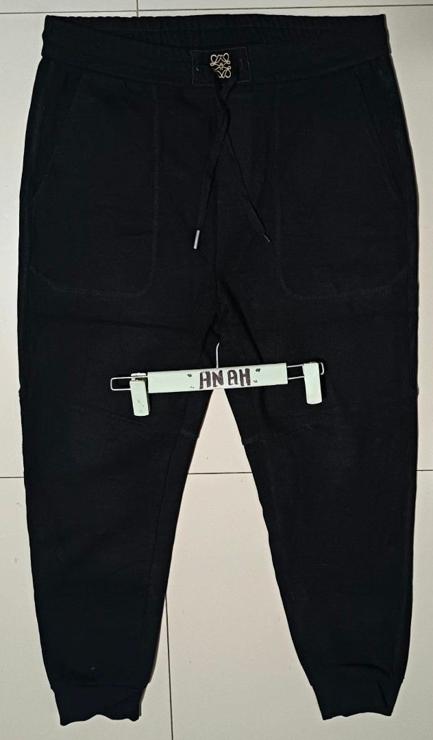 Black Jogger Pants with Embroidery (Category: Joggers) located in Valenzuela. Submitted by AnahThrift (Listing ID 1469061908, Image 3). Description: - Color: Solid black with gold and black stitching - Brand detail: Embroidered Loewe logo on the back pocket - Waist: Adjustable drawstring with branded hardware accents - Pockets: Functional front pockets - Cuffs: Comfortable ribbed ankle cuffs - Perfect for casual wear and daily styling.
