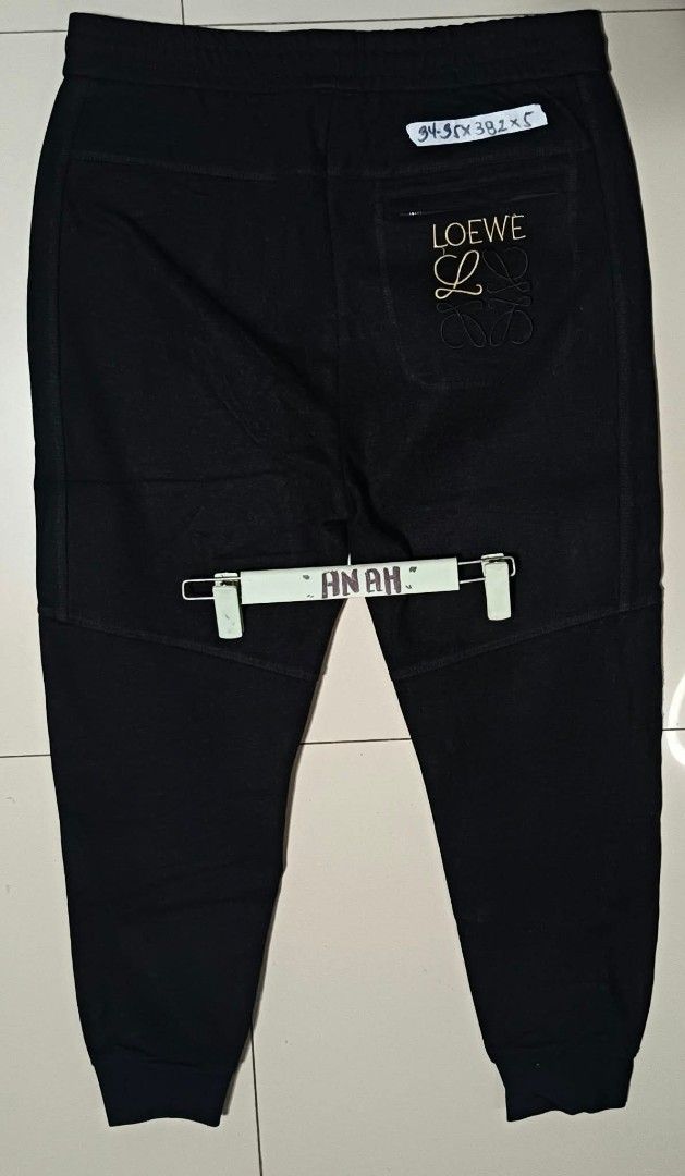 Black Jogger Pants with Embroidery (Category: Joggers) located in Valenzuela. Submitted by AnahThrift (Listing ID 1469061908, Image 2). Description: - Color: Solid black with gold and black stitching - Brand detail: Embroidered Loewe logo on the back pocket - Waist: Adjustable drawstring with branded hardware accents - Pockets: Functional front pockets - Cuffs: Comfortable ribbed ankle cuffs - Perfect for casual wear and daily styling.