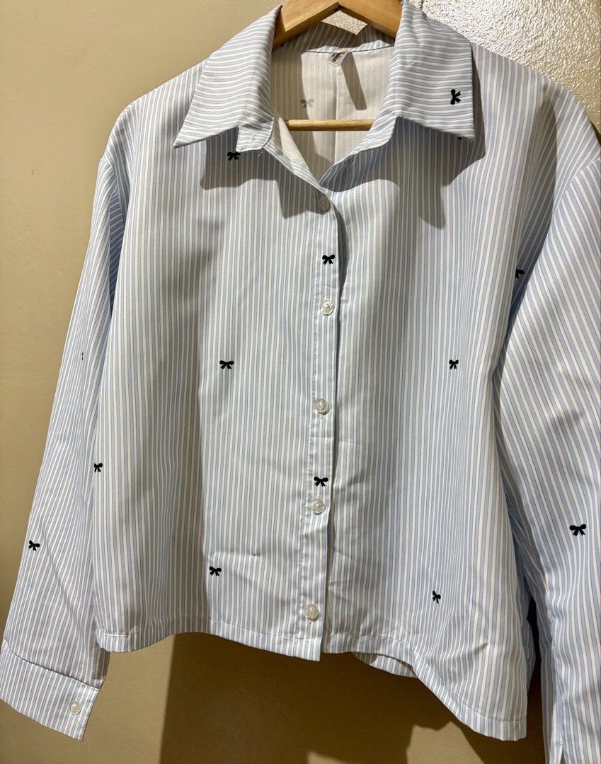 Blue and white striped button-down shirt with black bows (Category: Shirts) located in Caloocan City. Submitted by stella_mari27 (Listing ID 1469098861, Image 3). Description: - Style: Cropped long-sleeve button-down shirt - Design: Blue and white stripes with all-over black embroidered bow prints (even on collar and cuffs) - Fit: Regular fit with standard lapel collar and front button closure - Perfect for casual chic or preppy looks!.