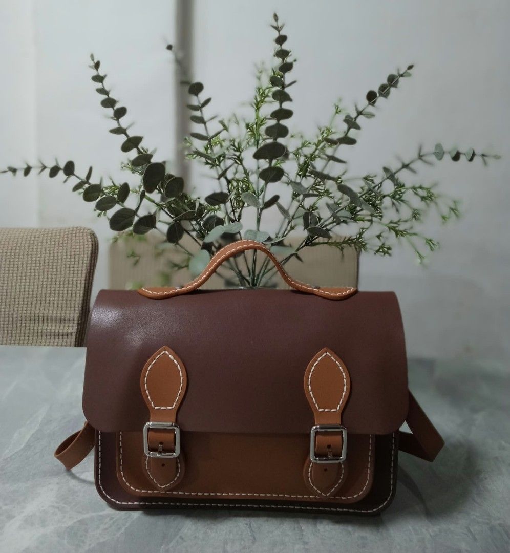 Brown Leather Satchel Crossbody Bag with Top Handle (Category: Cross-body Bags) located in Manila. Submitted by cosmiccloud-9236 (Listing ID 1468964310, Image 1). Description: - Two-tone brown leather satchel with a structured, boxy shape - Dual buckle strap closures on the front flap - Stylish white contrast stitching along the edges - Short top handle for hand carrying - Includes an adjustable long shoulder strap - Clean and minimalist back pan