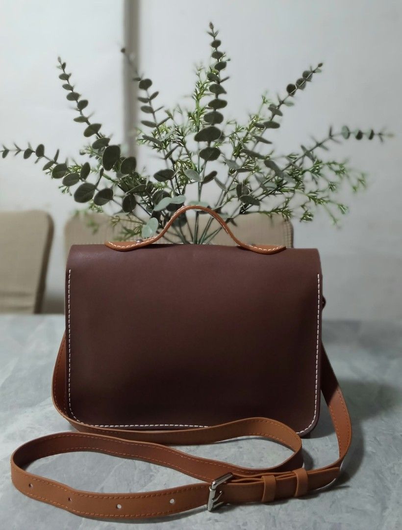 Brown Leather Satchel Crossbody Bag with Top Handle (Category: Cross-body Bags) located in Manila. Submitted by cosmiccloud-9236 (Listing ID 1468964310, Image 2). Description: - Two-tone brown leather satchel with a structured, boxy shape - Dual buckle strap closures on the front flap - Stylish white contrast stitching along the edges - Short top handle for hand carrying - Includes an adjustable long shoulder strap - Clean and minimalist back pan
