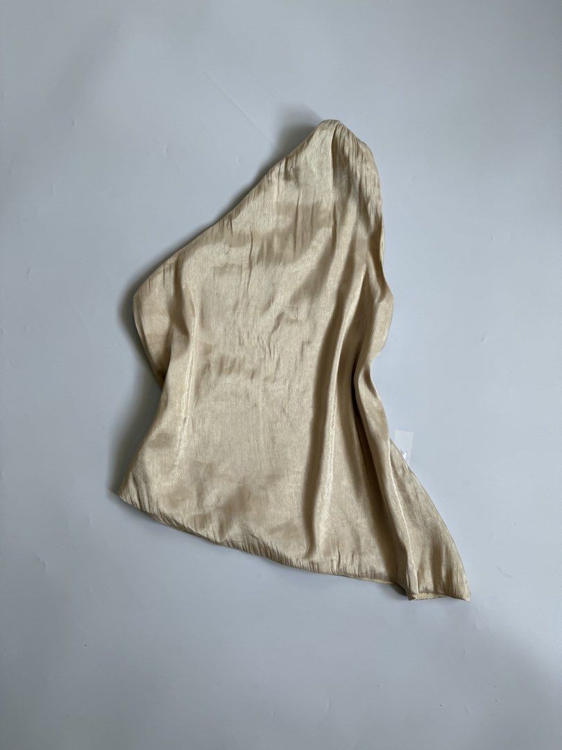 Champagne Satin One-Shoulder Asymmetric Top (Category: Sleeveless) located in Tarlac. Submitted by kr_closet (Listing ID 1468934459, Image 2). Description: - Color: Champagne gold tone - Style: One-shoulder neckline with trendy asymmetric hem - Material: Lightweight, silky fabric with a subtle sheen - Condition: Brand new with tag still attached, clean with no stains or pulls - Versatility: Easy to tuck into skirts or high-waisted pants.