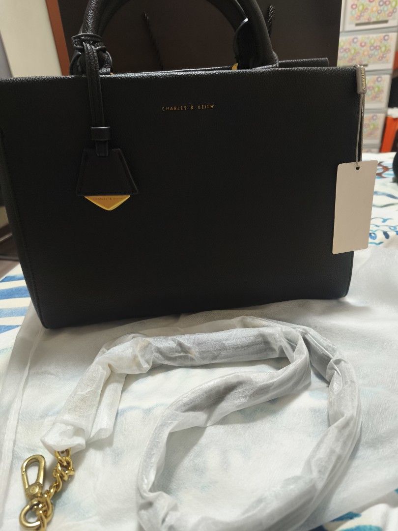 Charles & Keith Black Tote Handbag (Category: Tote Bags) located in San Jose. Submitted by jazees14 (Listing ID 1469038588, Image 2). Description: - Brand: Charles & Keith - Color: Classic Black - Condition: Brand new with original tags attached - Features: Clean pebbled finish, structured shape, and elegant gold lettering logo on the front - Straps: Sturdy top handles plus a detachable shoulder strap (still wrapped in protective plastic) - Versa