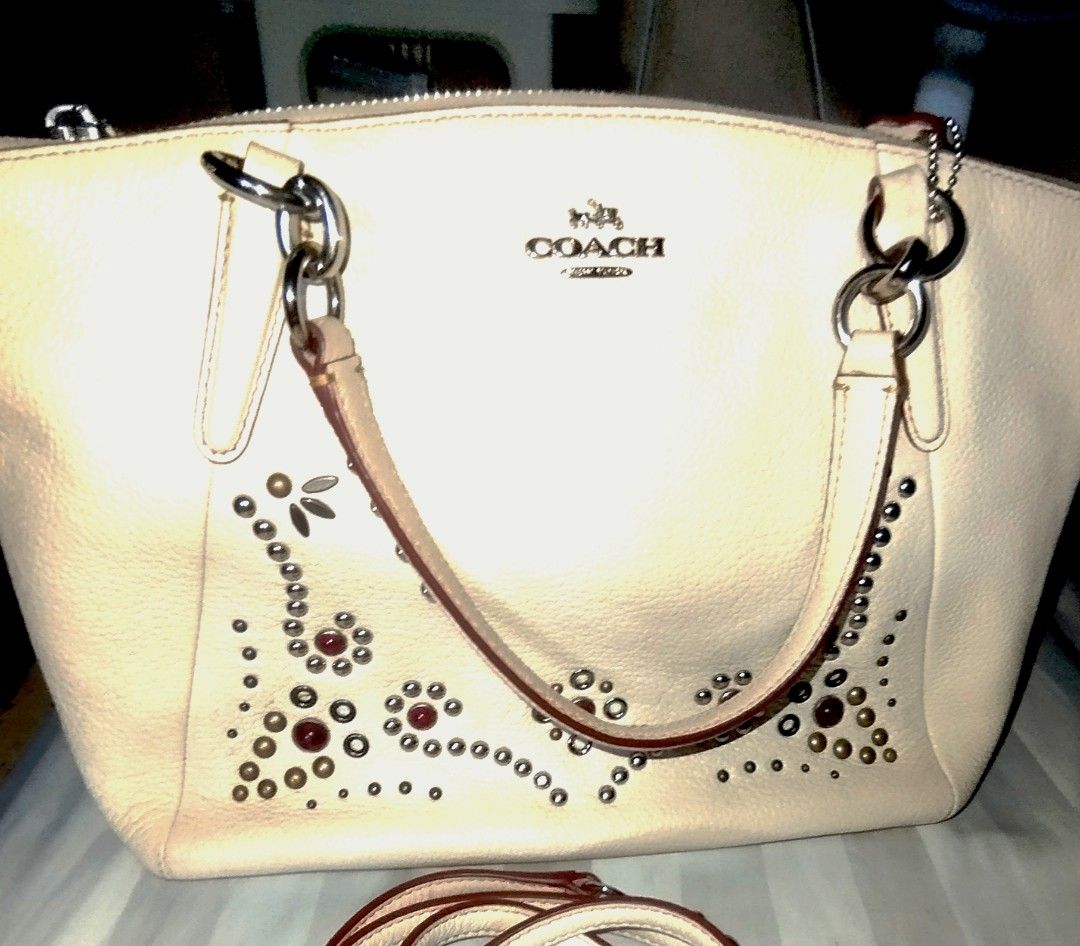 Coach White Leather Studded Handbag with Shoulder Strap (Category: Cross-body Bags) located in Manila. Submitted by lene48 (Listing ID 1469010482, Image 2). Description: - Authentic Coach handbag in versatile off-white pebbled leather - Stunning floral motif made with metallic studs and red cabochons - Silver-tone hardware with Coach horse and carriage logo - Dual top handles and a convenient detachable shoulder strap - Secure zip-top closure wit