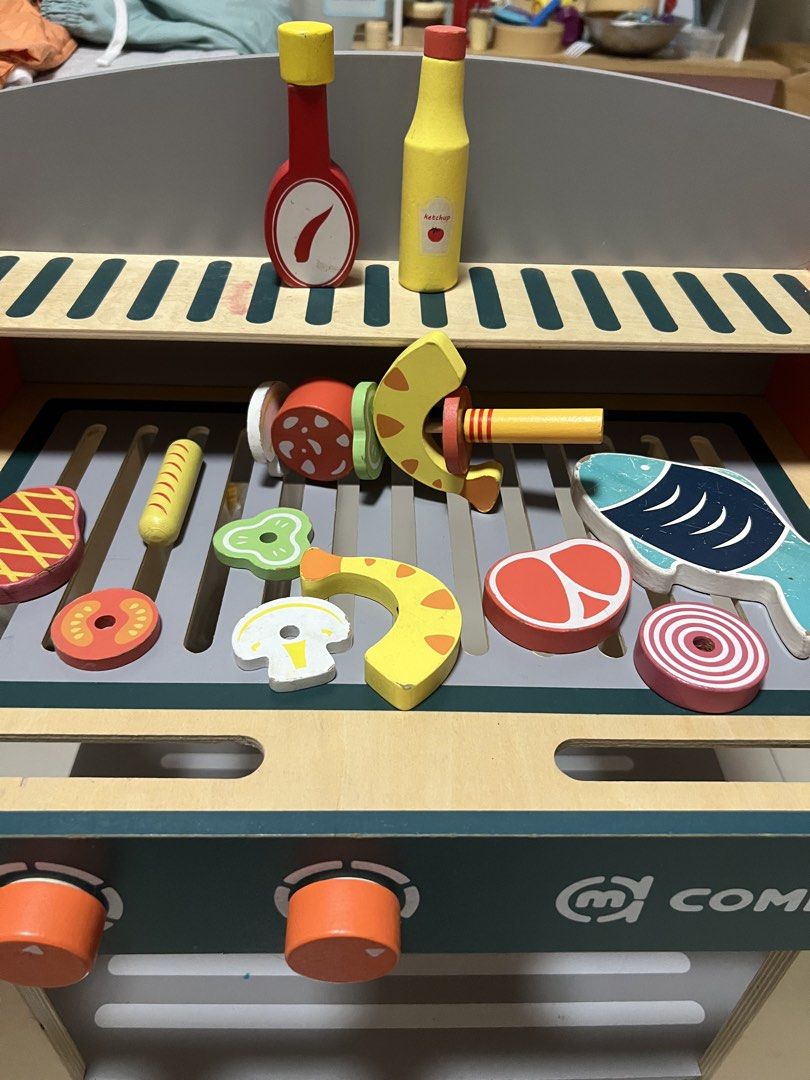 Commiki Wooden BBQ Grill Toy Set (Category: Kids Toys) located in Paranaque City. Submitted by heyoli (Listing ID 1469013780, Image 2). Description: - Brand: Commiki - Type: Wooden play barbecue set - Features interactive turning dials and a convenient storage shelf underneath - Includes magnetic play food (steak, fish, sausage, veggies) and condiment bottles - Great for engaging pretend play and developing fine motor skills.