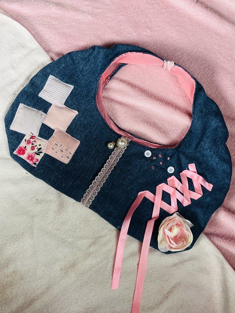 Denim handbag with pink ribbon and floral patchwork (Category: Tote Bags) located in Valenzuela. Submitted by closettee_ (Listing ID 1468954961, Image 1). Description: - Unique upcycled denim handbag with a handmade design - Front woven with pink satin ribbon and an artificial rose detail - Decorated with charming pearl buttons and ruffled lace trim down the middle - Finished with a pink fabric top edge lining - Features side patchwork squares in