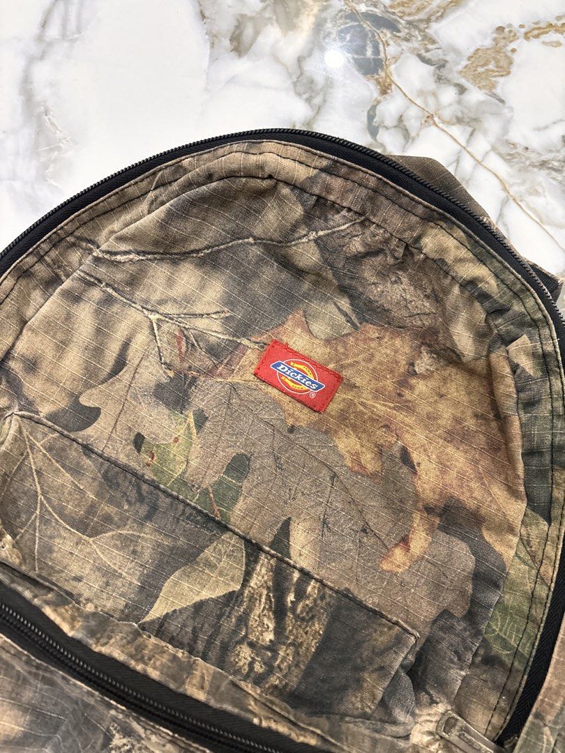 Dickies Mossy Oak Camo Backpack (Category: Backpacks) located in Cavite. Submitted by gelloots (Listing ID 1469047013, Image 3). Description: - Brand: Dickies - Pattern: Mossy Oak Camouflage - Storage: Classic front zip pocket for quick access - Details: Custom branded metal zipper pulls and iconic red Dickies logo patch - Comfort: Adjustable shoulder straps and padded backing - Condition: Great everyday carry for school, work, or outdoor trips.