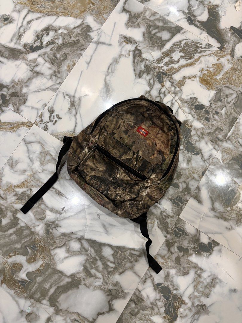 Dickies Mossy Oak Camo Backpack (Category: Backpacks) located in Cavite. Submitted by gelloots (Listing ID 1469047013, Image 1). Description: - Brand: Dickies - Pattern: Mossy Oak Camouflage - Storage: Classic front zip pocket for quick access - Details: Custom branded metal zipper pulls and iconic red Dickies logo patch - Comfort: Adjustable shoulder straps and padded backing - Condition: Great everyday carry for school, work, or outdoor trips.