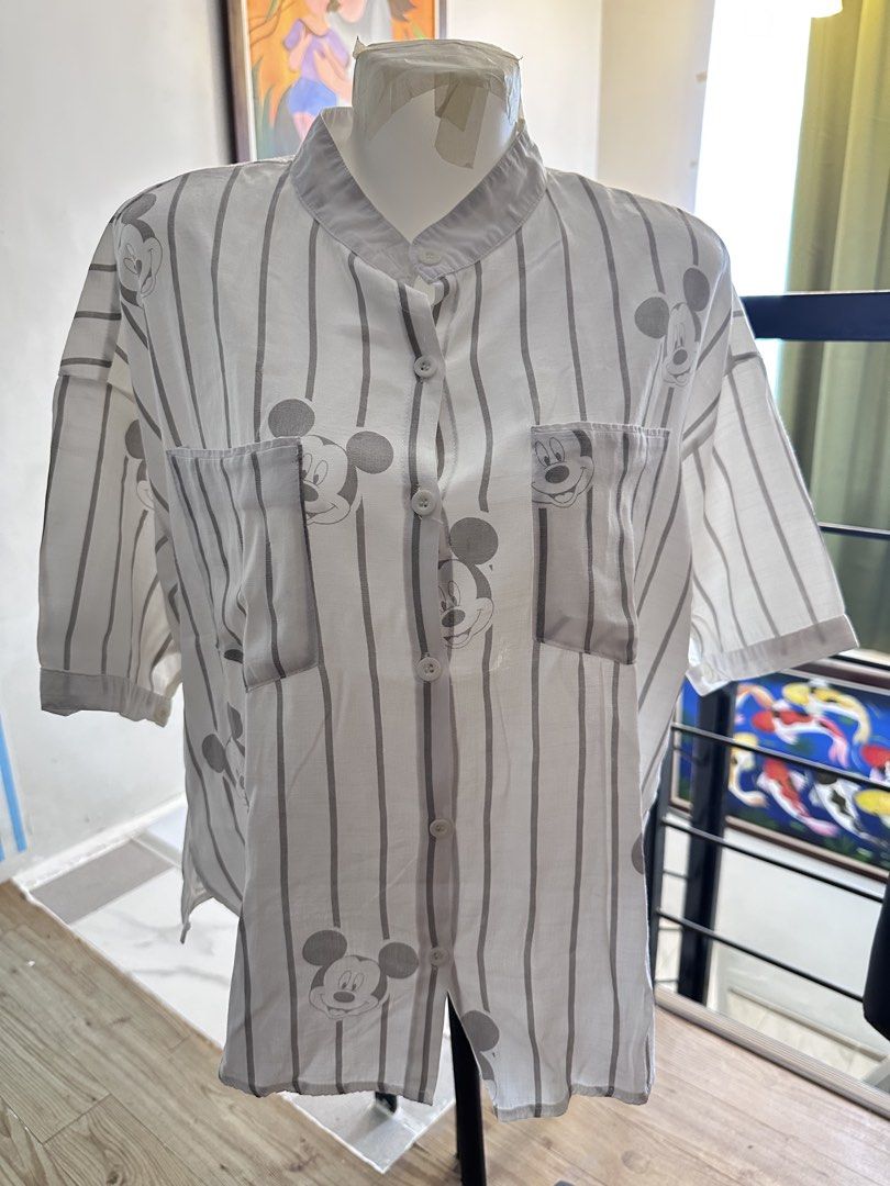 Disney Mickey Mouse Striped Button-Down Shirt (Category: Shirts) located in Manila. Submitted by rachael_23 (Listing ID 1469083798, Image 1). Description: - Design: White and grey stripes with all-over Mickey Mouse face prints - Style: Short sleeves, mandarin collar, and relaxed fit - Features: Two functional front chest pockets - Material: Lightweight and breathable fabric - Versatility: Easy to pair with jeans or shorts; great everyday wear for
