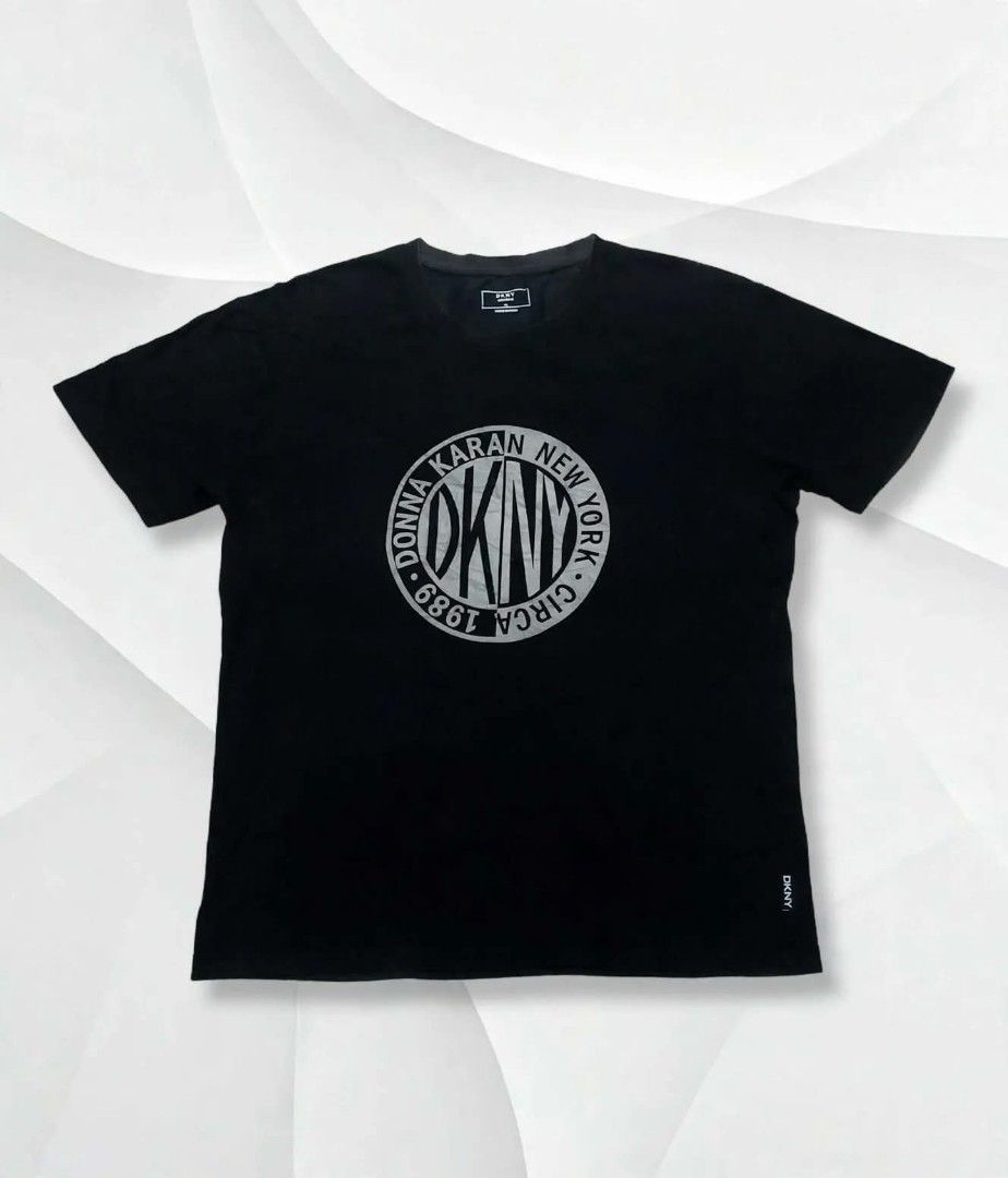 DKNY Black Logo T-Shirt I Tee (Category: Shirts) located in Aguinaldo. Submitted by ukayandthrift (Listing ID 1468958531, Image 1). Description: - Brand: DKNY - Color: Black - Design: Large circular logo graphic on front with small brand tag near hem - Cut: Crew neck, short sleeves - Fit: True to size, casual everyday wear - Condition: Brand new / Excellent.