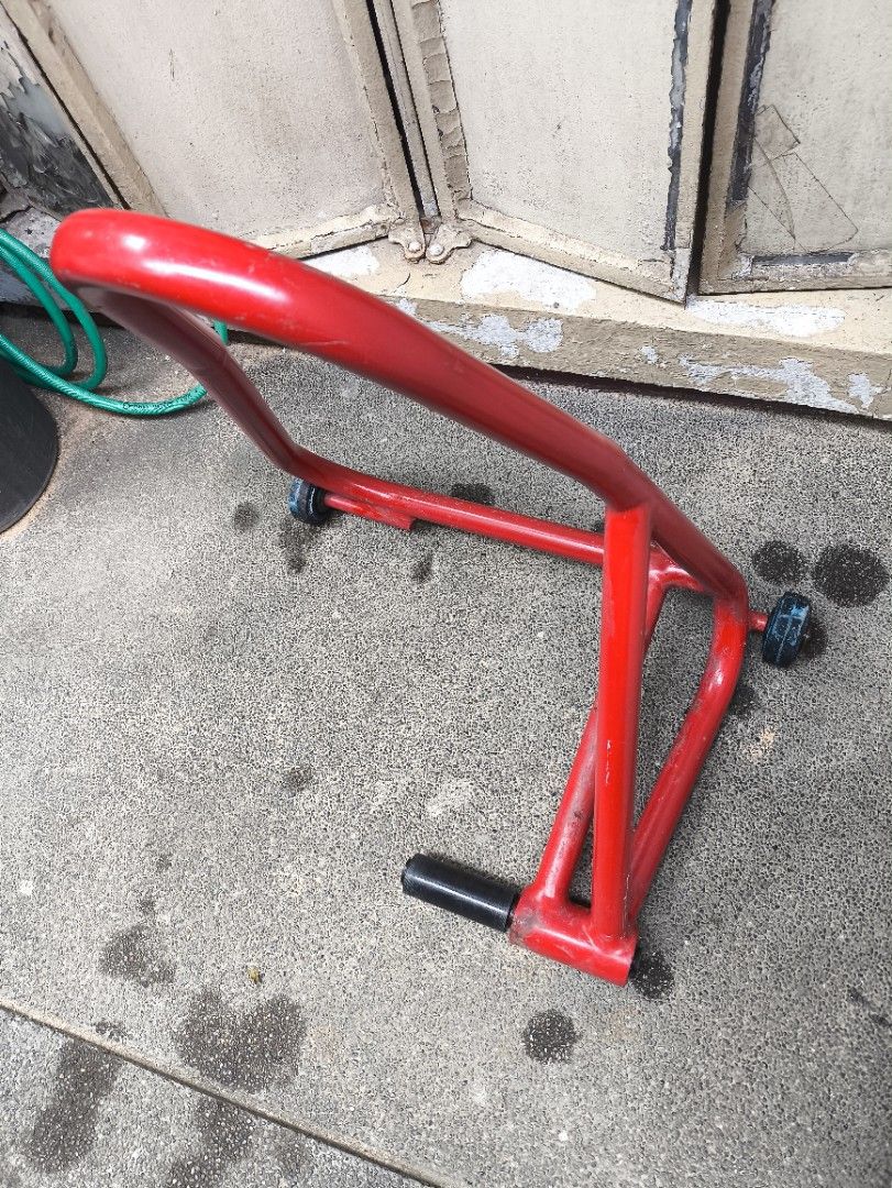 Ducati Motorcycle Rear Paddock Stand (Category: Bicycles) located in Pasig City. Submitted by giarpo (Listing ID 1469056674, Image 1). Description: - Red steel rear paddock stand for motorcycles - Measures ~21 cm across the lifting pin - Sturdy build with small black wheels for easy rolling - Shows minor scuffs and paint chips from normal workshop use - 100% solid and fully functional for maintenance and chain cleaning.