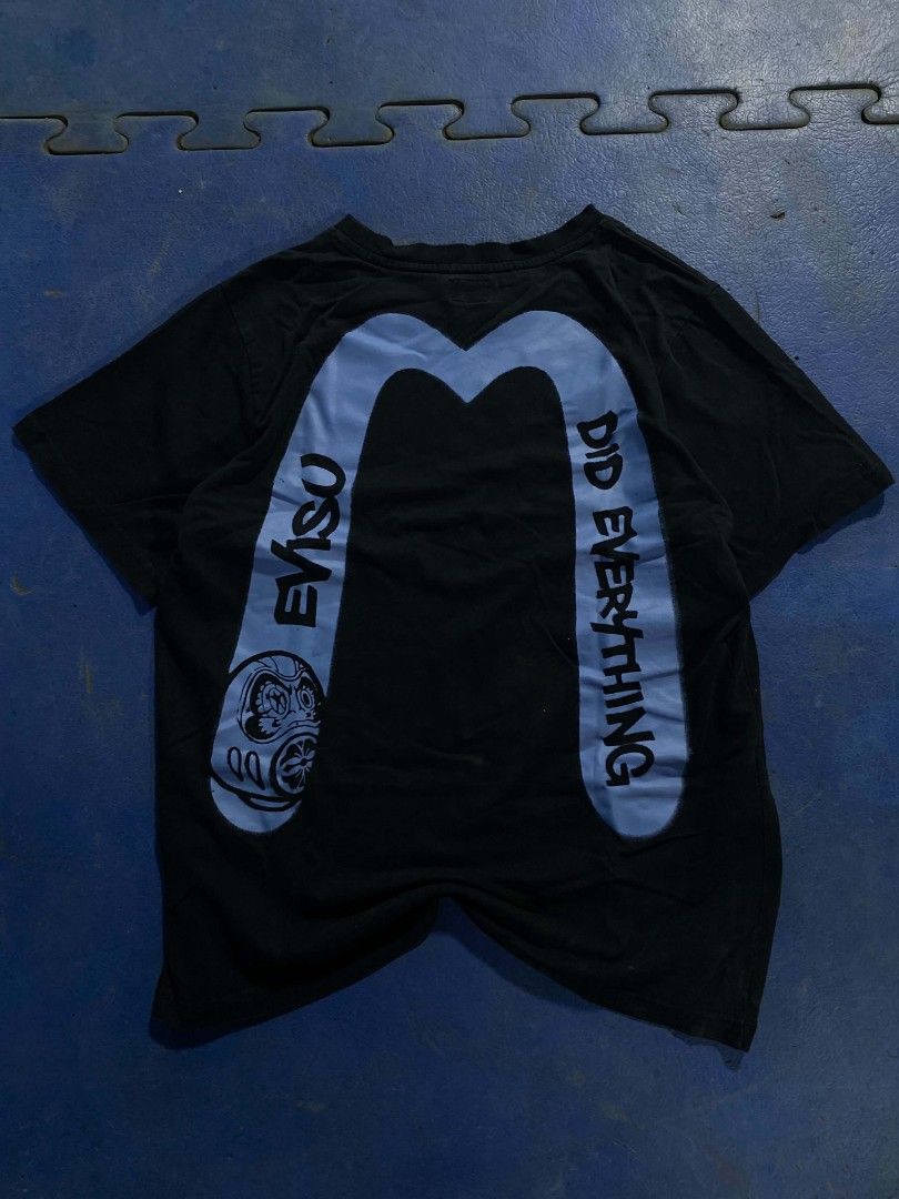 Evisu Black Graphic T-Shirt Size M (Category: Tshirts & Polo Shirts ) located in Manila. Submitted by jessieboym36298 (Listing ID 1468946727, Image 2). Description: - Brand: Evisu - Color: Black with light blue graphics - Size: Medium (M) - Fit: Regular fit, short sleeves - Design: Graffiti style logo on front chest, large signature print with Daruma mask detail on back - Condition: Clean fabric with bright, vibrant graphics - Style: Streetwear /