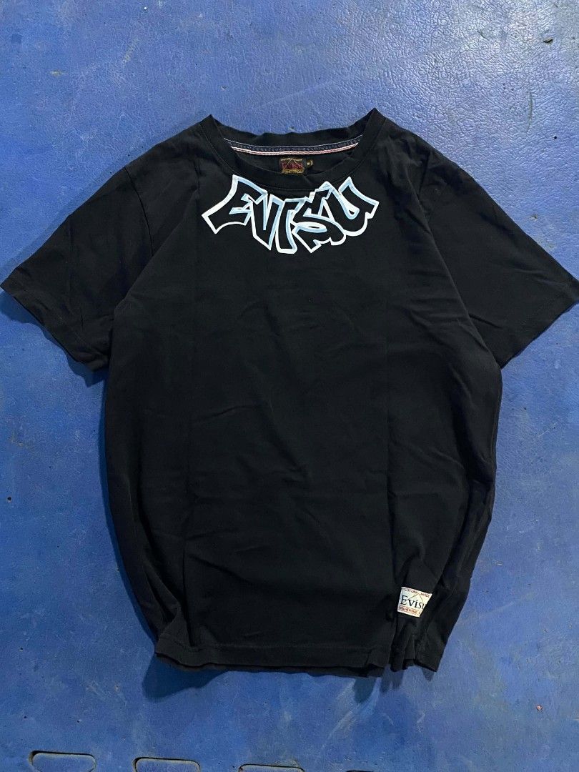 Evisu Black Graphic T-Shirt Size M (Category: Tshirts & Polo Shirts ) located in Manila. Submitted by jessieboym36298 (Listing ID 1468946727, Image 3). Description: - Brand: Evisu - Color: Black with light blue graphics - Size: Medium (M) - Fit: Regular fit, short sleeves - Design: Graffiti style logo on front chest, large signature print with Daruma mask detail on back - Condition: Clean fabric with bright, vibrant graphics - Style: Streetwear /