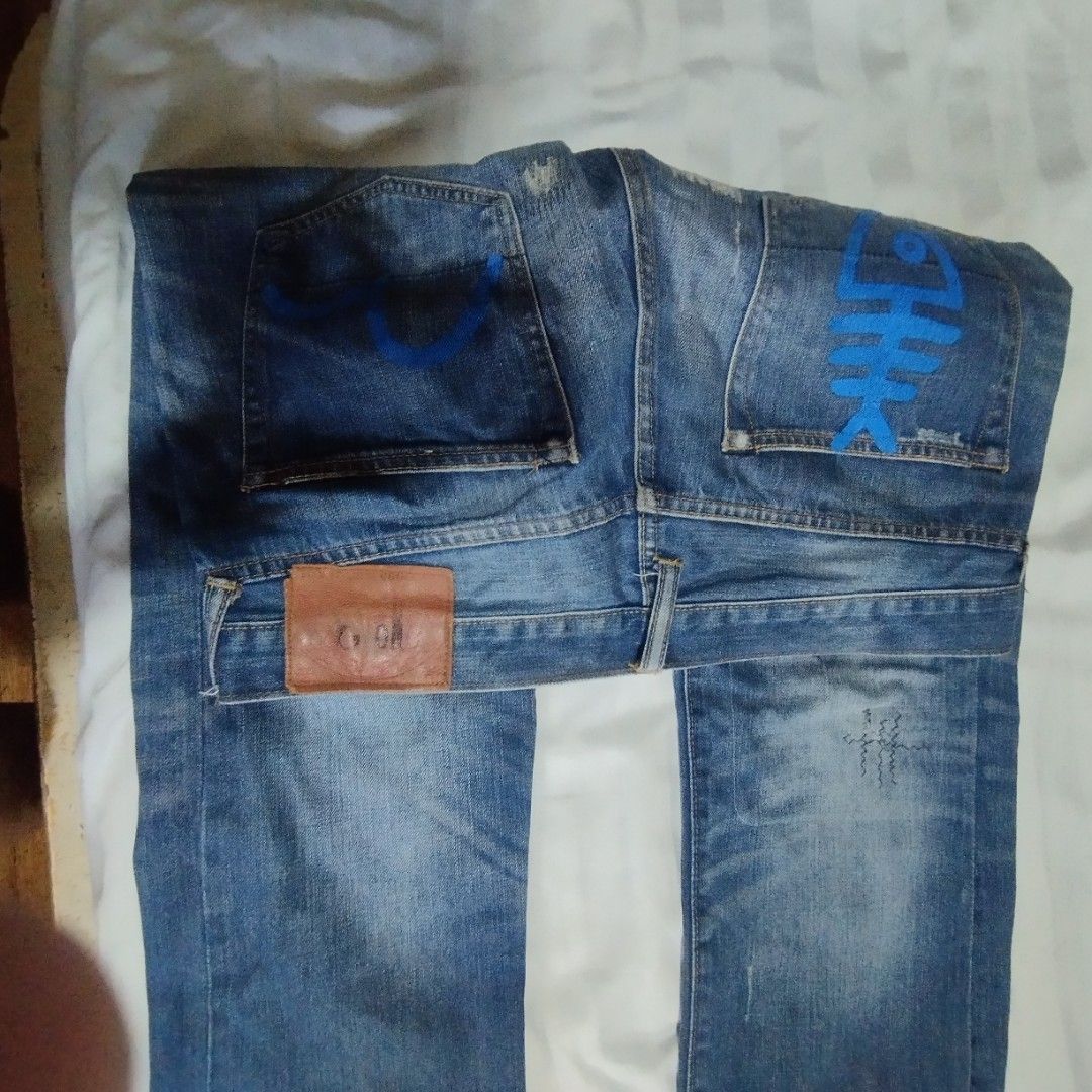 Evisu Blue Distressed Denim Jeans (Category: Jeans) located in Manila. Submitted by lene48 (Listing ID 1468937752, Image 2). Description: - Brand: Evisu - Color/Wash: Blue faded wash with distressed and patched details - Fit: Regular fit, straight leg cut - Closure: Classic button fly - Unique Design: Painted blue graphics with fish skeleton on back pockets - Branded Details: Inside waistband text, printed pocket lining, and back leather patch - 