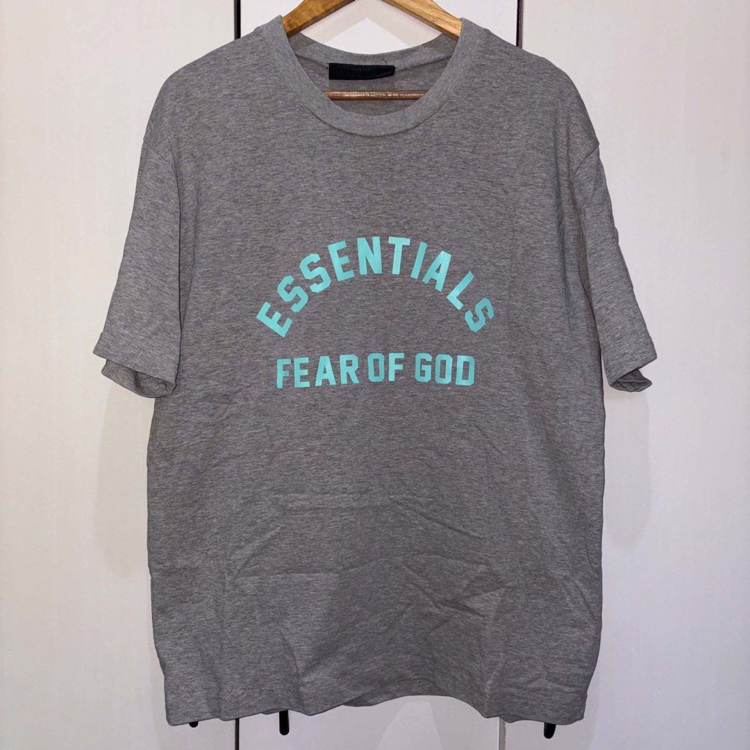 Fear of God Essentials Grey (Category: Tshirts & Polo Shirts ) located in Rosario. Submitted by elyukano2506 (Listing ID 1469021168, Image 1). Description: - Brand: Fear of God Essentials - Color: Grey with Turquoise Logo - Size: Large-XL - Material: 100% heavy cotton, Made in Vietnam - Details: Arched chest branding, black rubber label at back collar - Condition: Clean fabric, crew neck, short sleeves.