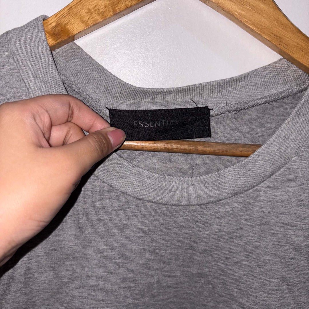 Fear of God Essentials Grey (Category: Tshirts & Polo Shirts ) located in Rosario. Submitted by elyukano2506 (Listing ID 1469021168, Image 2). Description: - Brand: Fear of God Essentials - Color: Grey with Turquoise Logo - Size: Large-XL - Material: 100% heavy cotton, Made in Vietnam - Details: Arched chest branding, black rubber label at back collar - Condition: Clean fabric, crew neck, short sleeves.