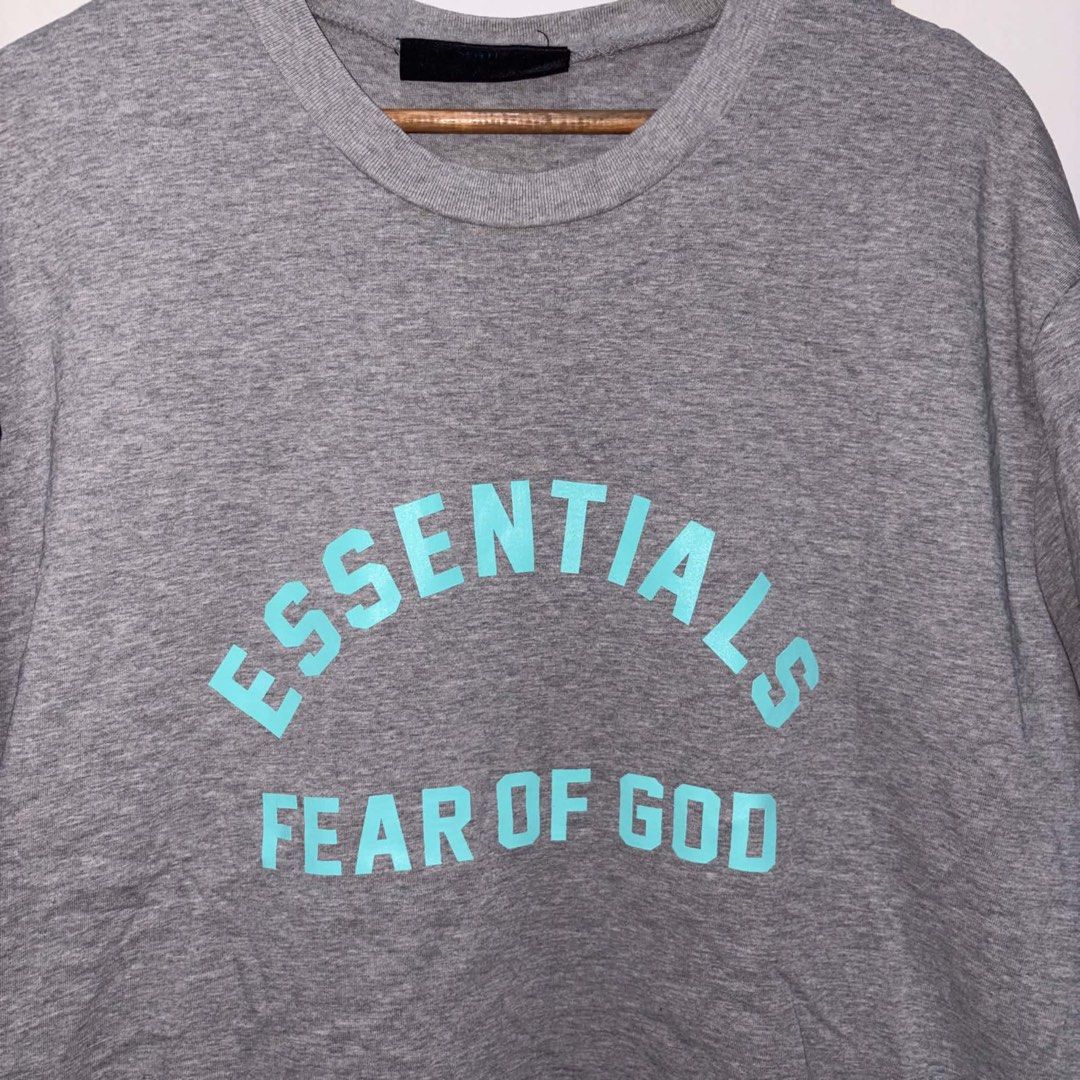Fear of God Essentials Grey (Category: Tshirts & Polo Shirts ) located in Rosario. Submitted by elyukano2506 (Listing ID 1469021168, Image 3). Description: - Brand: Fear of God Essentials - Color: Grey with Turquoise Logo - Size: Large-XL - Material: 100% heavy cotton, Made in Vietnam - Details: Arched chest branding, black rubber label at back collar - Condition: Clean fabric, crew neck, short sleeves.