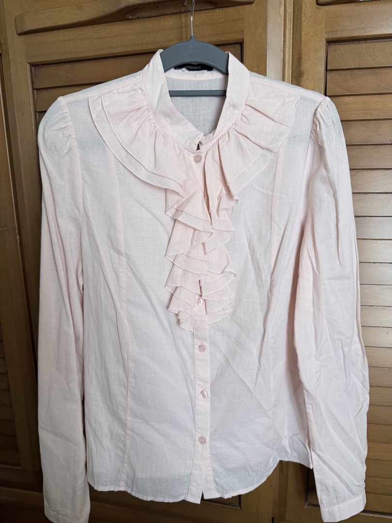 Forever 21 Light Pink Ruffled Long Sleeve Blouse (Category: Longsleeves) located in Paranaque City. Submitted by roanclauds (Listing ID 1468957023, Image 1). Description: - Brand: Forever 21 - Color: Pale pink with tonal buttons - Material: Soft, comfortable fabric - Design: Long sleeves, layered front ruffles, stand-up collar, and shoulder gathers on the back - Fit: Standard fit - Condition/Occasion: Great for work or casual outings.