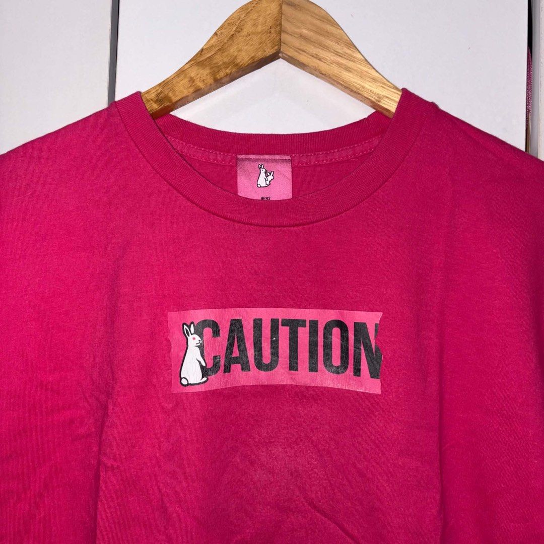 FR2 Caution Pink T-Shirt (Category: Tshirts & Polo Shirts ) located in Rosario. Submitted by elyukano2506 (Listing ID 1469021752, Image 2). Description: - Brand: FR2 - Color: Bright Pink - Size: Medium - Material: 100% Cotton - Design: Large CAUTION rabbit graphic on chest, small embroidered rabbit patch near hem - Details: Crew neck, short sleeves, solid pink back, original collar tag and care label - Condition: Excellent / Pre-loved (ready to w