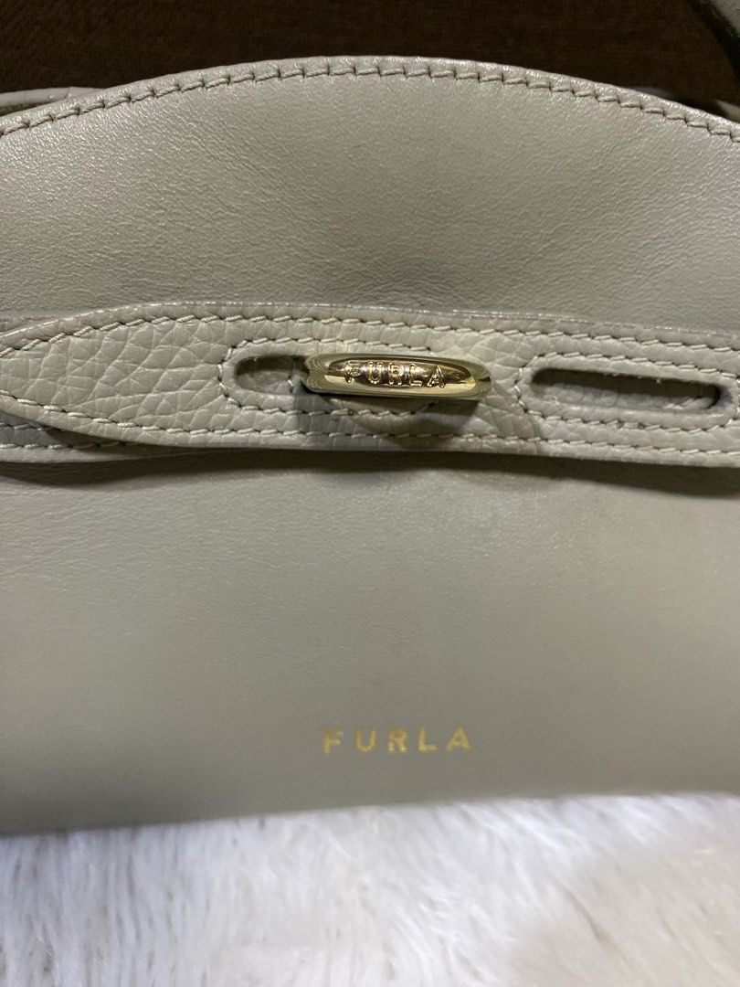 Furla bag (Category: Purses & Pouches) located in San Antonio. Submitted by clinicallycute_. (Listing ID 1469047571, Image 2). Description: - Brand: Furla - Material: Genuine leather in neutral beige - Hardware: Elegant gold accents with front strap closure - Design: Structured silhouette with a single top handle - Interior: Fabric-lined with 'Made in Italy' and 'Genuine Leather' brand patch - Size: Compact, ideal for daily essentials - Condition