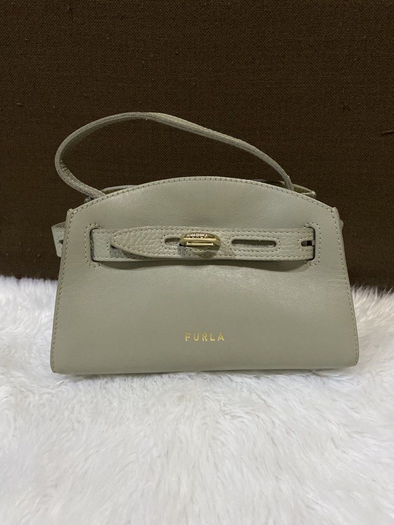 Furla bag (Category: Purses & Pouches) located in San Antonio. Submitted by clinicallycute_. (Listing ID 1469047571, Image 1). Description: - Brand: Furla - Material: Genuine leather in neutral beige - Hardware: Elegant gold accents with front strap closure - Design: Structured silhouette with a single top handle - Interior: Fabric-lined with 'Made in Italy' and 'Genuine Leather' brand patch - Size: Compact, ideal for daily essentials - Condition