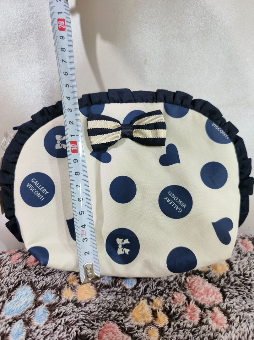 Gallery Visconti Polka Dot Pouch Bag (Category: Purses & Pouches) located in San Leonardo. Submitted by burgossanleonardo.12345 (Listing ID 1469081155, Image 3). Description: - Brand: Gallery Visconti - Condition: Brand new with original store tag (Style 928423) - Design: Cream base with navy blue polka dots and heart graphics - Details: Navy ruffle trim on top and an adorable striped bow on the front - Measurements: Approx. 25cm (L) x 20cm (H) -