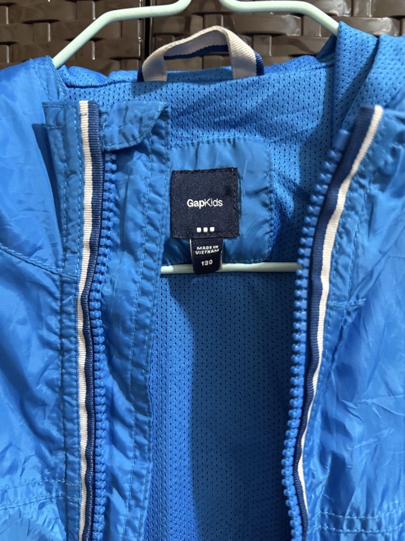 GapKids Blue Windbreaker Jacket Size 130 (Category: Tshirts & Polo Shirts ) located in Manila. Submitted by vastwind-676c (Listing ID 1468957087, Image 3). Description: - Brand: GapKids - Size: 130 - Color: Bright blue - Material: Lightweight with breathable mesh lining - Features: Full zip closure with white trim, attached hood, front pockets, and Gap 1969 logo near the hem - Origin: Made in Vietnam - Condition: Great for outdoor activities and 