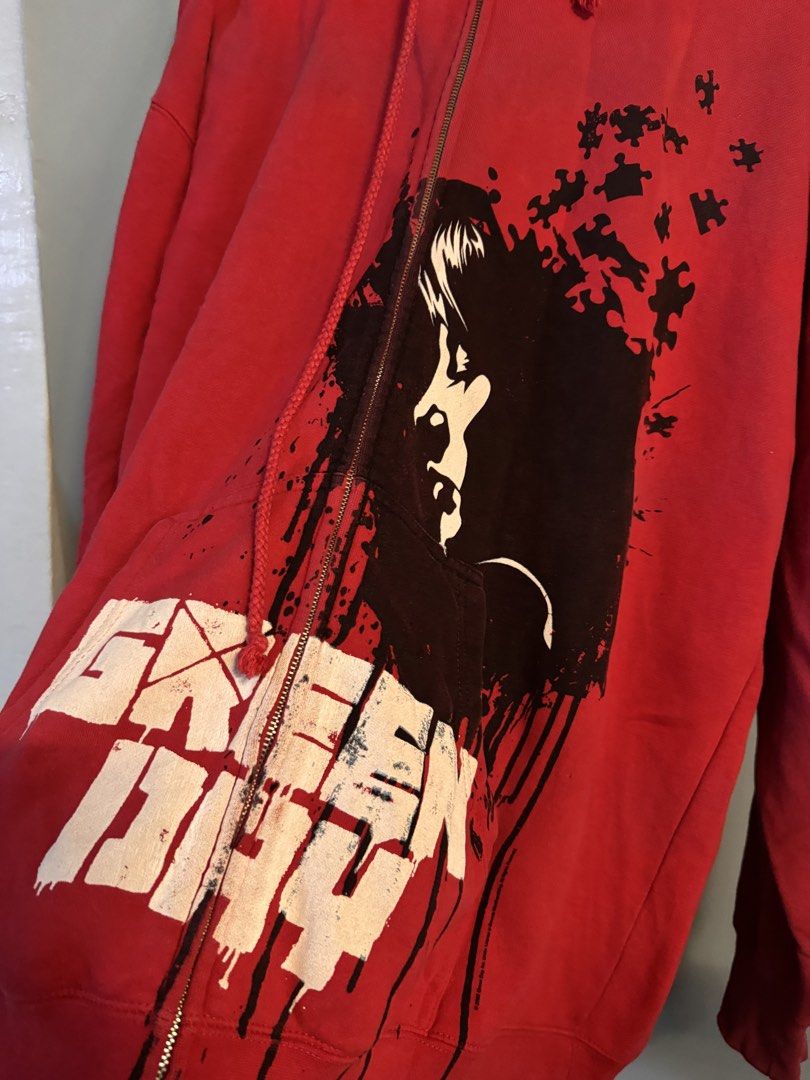Green Day Red Zip-Up Hoodie (Category: Hoodies) located in Alaminos. Submitted by outfitcheck.ph (Listing ID 1469102483, Image 2). Description: - Brand/Style: Official Green Day band merch red zip-up hoodie - Size: XL - Design: Striking black and white graphic portrait with puzzle piece accents and distressed band lettering at the pocket - Material: 80% cotton, 20% polyester - Features: Adjustable drawstring hood and full front metal zipper - Con