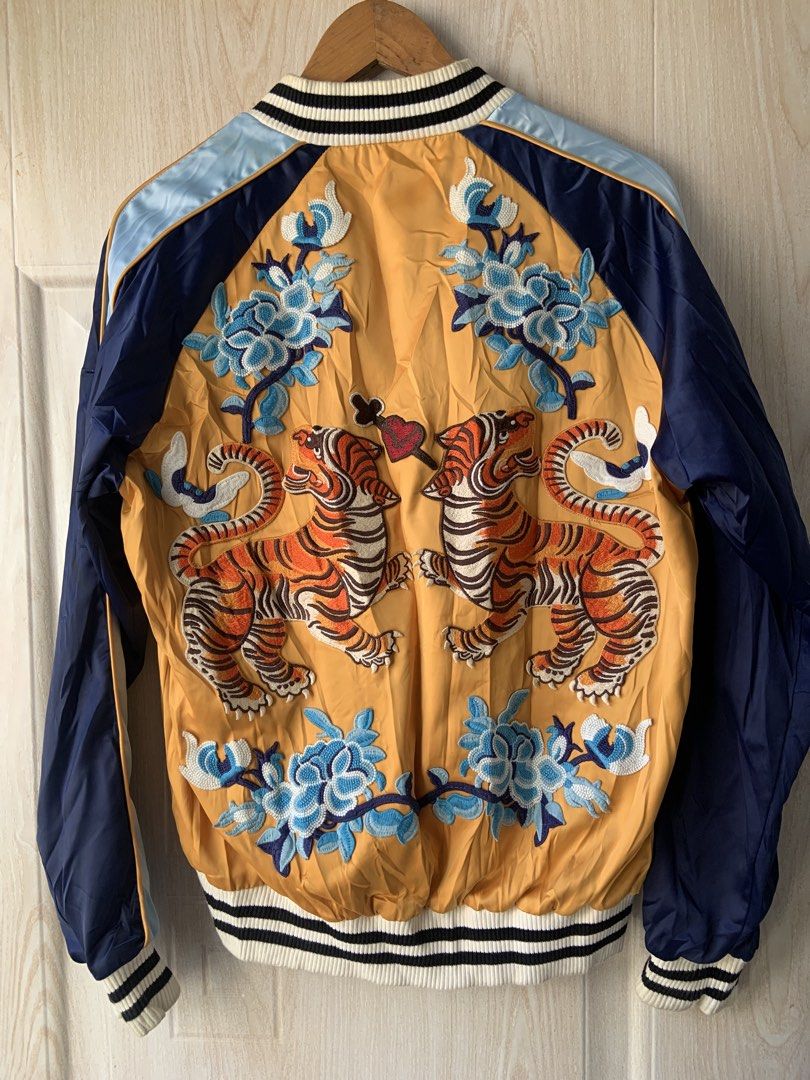 Gucci Bomber Jacket Tiger Embroidery Size L (Category: Coats, Jackets and Outerwear) located in Angeles City. Submitted by manlapidma26771 (Listing ID 1468977156, Image 2). Description: Gucci bomber jacket in gold, navy, and light blue. Size large. Front zipper closure with Gucci pull tab. Large glittery 'M' applique on the chest. Detailed tiger and floral embroidery across the back panel. Striped ribbed collar, cuffs, and hem. Synthetic material