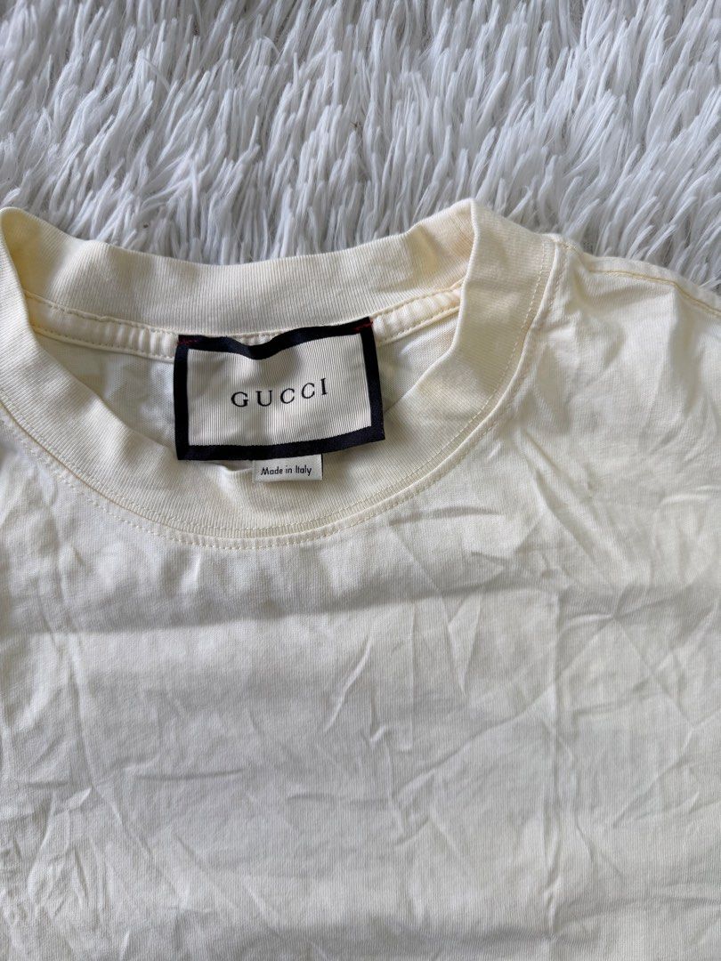 Gucci White Graphic T-Shirt (Category: Tshirts & Polo Shirts ) located in Pasig City. Submitted by dabeee07 (Listing ID 1468952068, Image 2). Description: - Gucci t-shirt made in Italy - Color: Cream-coloured - Design: Distressed rose sketch on lower front, large logo sketch and handwritten Gucci lettering on upper back - Fit/Style: Classic crew neck, short sleeves, straight hem - Condition: Brand labels and fabric care tags attached - Mode of Pa