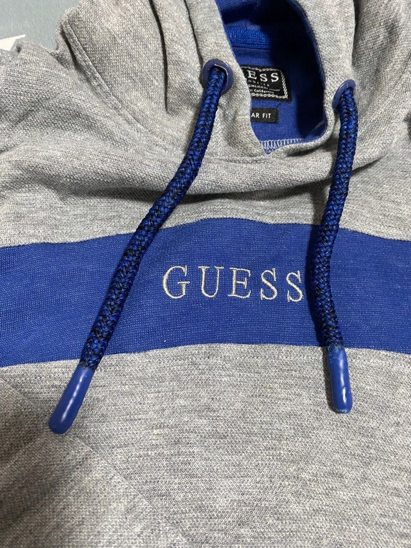 Guess Grey Blue Pullover Hoodie Regular Fit (Category: Coats, Jackets and Outerwear) located in Taguig. Submitted by maaarrrrrcky (Listing ID 1469011716, Image 3). Description: - Brand: Guess - Color: Grey and Blue - Fit: Regular fit, soft and comfortable material - Design: Blue drawstring hood with thick braided cords, matching blue chest stripe, and embroidered white Guess logo - Pockets: Front kangaroo pocket with secure zippered closures - De