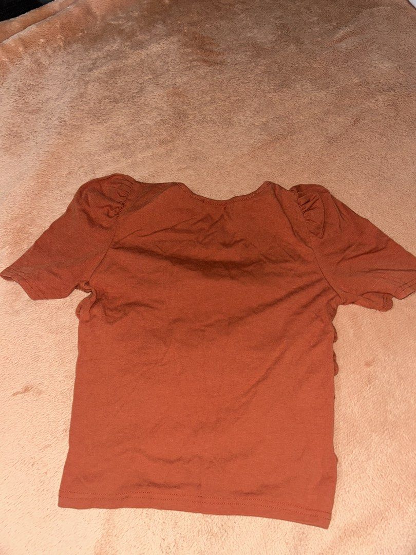 GUHUI rust orange ruched puff sleeve top (Category: Blouses) located in Manila. Submitted by prelovedbyanavi (Listing ID 1468956386, Image 2). Description: - Brand: GUHUI - Color: Rust orange (great for autumn/fall) - Neckline: Square neckline with 4 decorative metal buttons - Sleeves: Puff sleeves for added shoulder shape - Fit: Fully ruched down the front sides for a fitted look; plain back - Material: Soft and stretchy fabric.