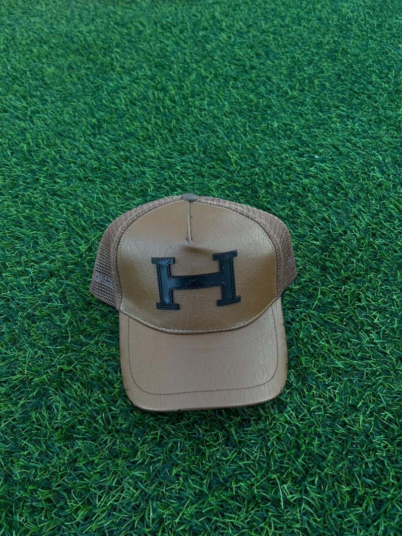 Hermes Brown Leather H Logo Trucker Hat Cap (Category: Caps & Hats) located in Pasig City. Submitted by paulclzdo (Listing ID 1469064972, Image 1). Description: - Style: Classic trucker hat - Front: Brown faux leather with black embroidered H logo - Back: Breathable mesh with adjustable snapback closure - Interior: Hermès branded sweatband taping and care tag - Condition: Great piece to elevate your daily outfits - Shipping or meetups available a