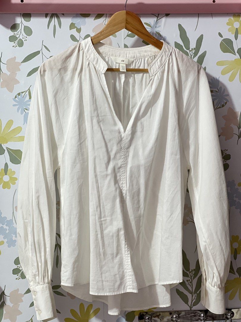H&M White V-Neck Blouse Size M oversized (Category: Blouses) located in Pasig City. Submitted by morilove (Listing ID 1469054566, Image 1). Description: - Brand: H&M - Size: M - Color: White - Neckline: Split V-neck with mandarin collar - Sleeves: Long sleeves with buttoned cuffs and gathered detailing - Hem: Curved hem - Material: Lightweight fabric - Condition: Clean and well-maintained - Style: Classic casual staple, perfect for work or weeken