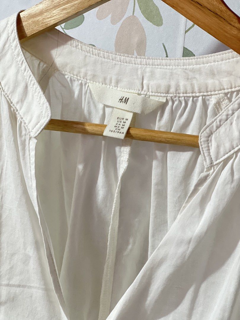 H&M White V-Neck Blouse Size M oversized (Category: Blouses) located in Pasig City. Submitted by morilove (Listing ID 1469054566, Image 2). Description: - Brand: H&M - Size: M - Color: White - Neckline: Split V-neck with mandarin collar - Sleeves: Long sleeves with buttoned cuffs and gathered detailing - Hem: Curved hem - Material: Lightweight fabric - Condition: Clean and well-maintained - Style: Classic casual staple, perfect for work or weeken