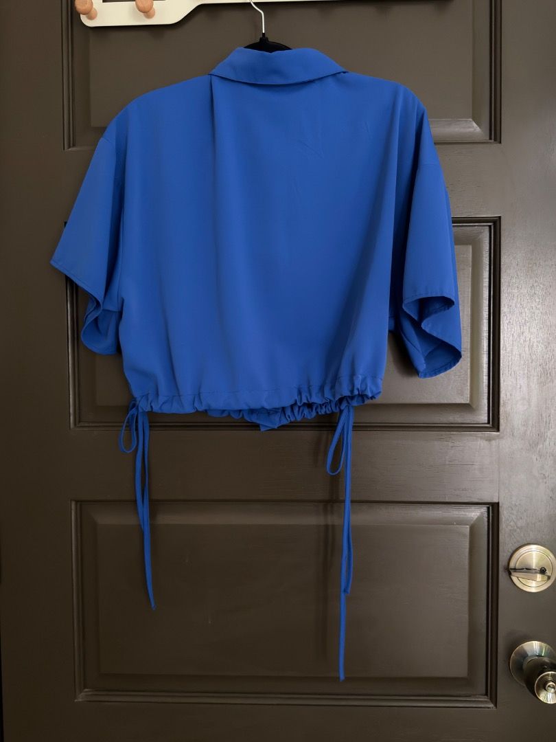 HYFVE Royal Blue Button Up Crop Blouse (Category: Blouses) located in Calamba. Submitted by prongsiepoo (Listing ID 1469079736, Image 2). Description: - Brand: Hyfve - Color: Bright royal blue - Fit: Relaxed fit through the body - Details: Collared neck, short sleeves, and two front chest pockets - Feature: Adjustable drawstring hem for waist cinching - Material: Lightweight fabric.