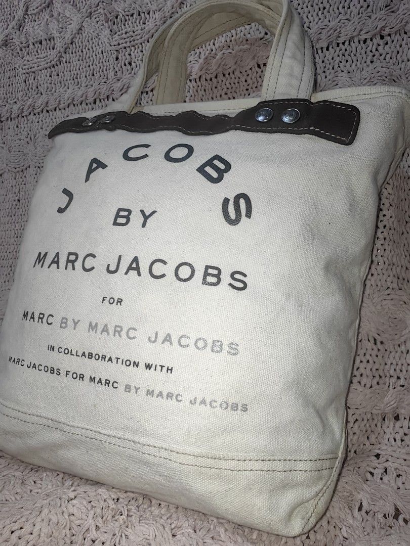 JACOBS BY MARC JACOBS Canvas Tote Bag (Category: Luxury Bags & Wallets) located in Tuguegarao City. Submitted by ekko_bag (Listing ID 1468935464, Image 3). Description: Item Specifics: Condition - In Very Good condition. ...NEED WASH... Thrifted from Japanese Bale ✔️✔✔ Marc Jacobs off-white/ivory canvas tote bag featuring dark brown suede-like top trim with silver snap details and stacked "JACOBS BY MARC JACOBS" typography on the front. ✔️✔✔ 🚫Ne