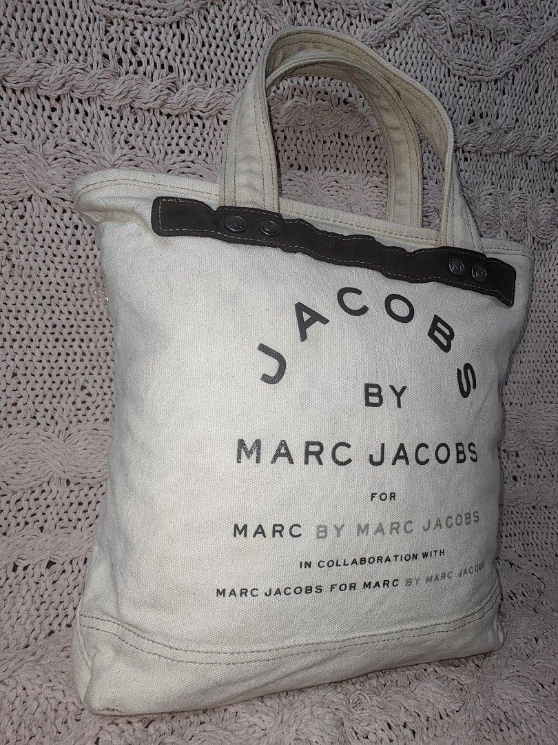JACOBS BY MARC JACOBS Canvas Tote Bag (Category: Luxury Bags & Wallets) located in Tuguegarao City. Submitted by ekko_bag (Listing ID 1468935464, Image 2). Description: Item Specifics: Condition - In Very Good condition. ...NEED WASH... Thrifted from Japanese Bale ✔️✔✔ Marc Jacobs off-white/ivory canvas tote bag featuring dark brown suede-like top trim with silver snap details and stacked "JACOBS BY MARC JACOBS" typography on the front. ✔️✔✔ 🚫Ne