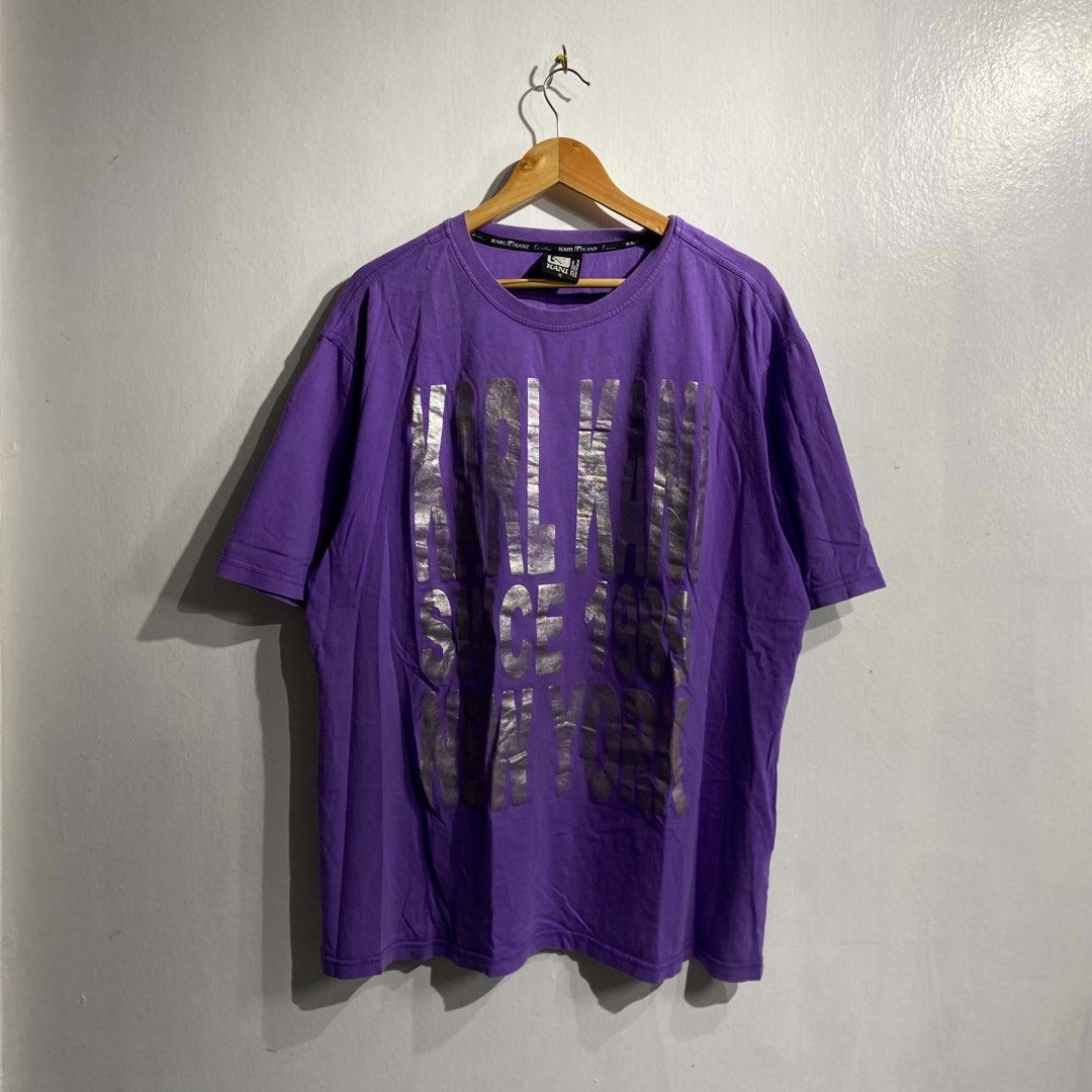 Karl Kani Purple Graphic Tee (Category: Shirts) located in Roxas City. Submitted by vaultcultureco. (Listing ID 1469094077, Image 1). Description: - Brand: Karl Kani - Size: XL - Color: Purple with large silver foil front lettering (Since 1989 New York) - Material: 100% Cotton - Fit/Style: Short sleeves, crew neckline, casual streetwear - Condition: Excellent.