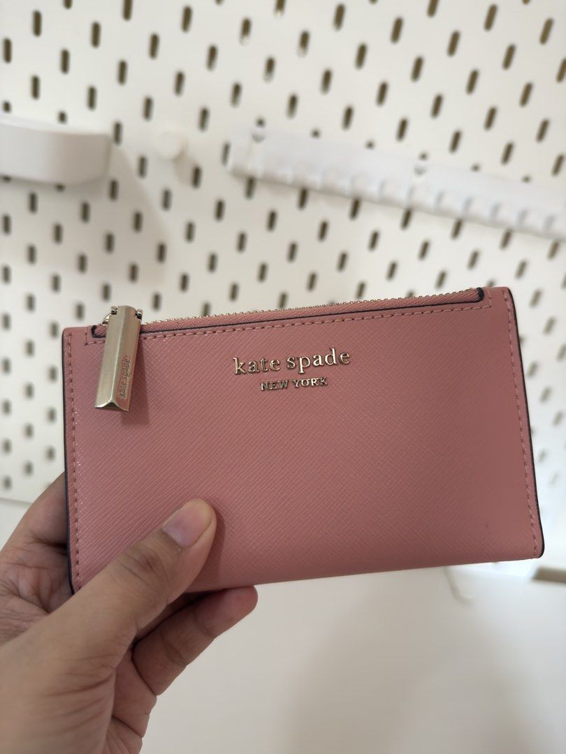 Kate Spade Pink Bifold Wallet (Category: Wallets & Card holders) located in Bacoor. Submitted by katie_tephanii (Listing ID 1468941794, Image 2). Description: - Brand: Kate Spade New York - Color: Dusty pink with light beige interior - Hardware: Gold-tone with front logo lettering - Compartments: Multiple card slots, ID window, and a convenient top zip pocket - Size: Compact and lightweight, easily fits in mini bags - Condition: Brand new / Excel