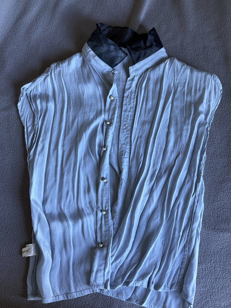 Light blue sleeveless button-up blouse with black contrasting collar (Category: Blouses) located in Pasig City. Submitted by laagn.ph (Listing ID 1469088993, Image 1). Description: - Color: Light blue with contrasting black patterned collar - Design: Sleeveless, button-up front with elegant pearl-style buttons - Fit: Relaxed, draped fit through the body - Fabric: Lightweight with a slight sheen - Styling: Ideal with high-waisted skirts or trouser