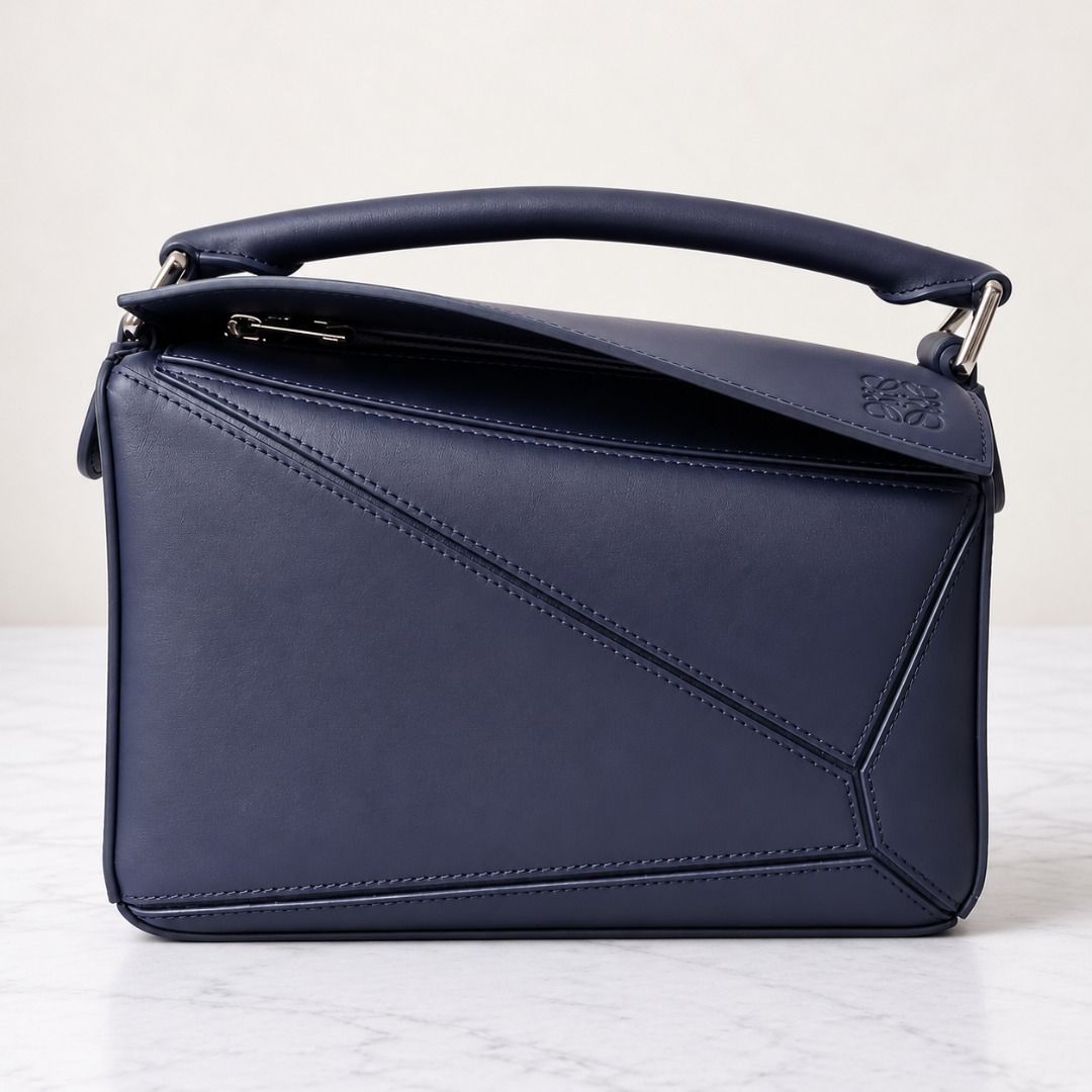 Loewe Puzzle Small Bag Navy Blue (Category: Luxury Bags & Wallets) located in Cebu City. Submitted by theluxxaffair (Listing ID 1429484766, Image 1). Description: Loewe Classic Puzzle Small bag crafted in navy blue smooth satin calfskin leather with palladium-tone hardware. Features a top handle, detachable shoulder strap with the Loewe logo, and zipper closure. Finished with the signature geometric leather panels and embossed Loewe logo on the s