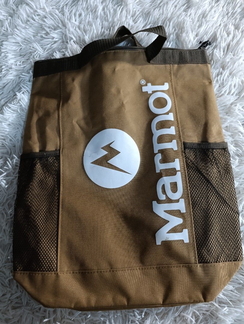 Marmot Brown Backpack Tote Bag with Mesh Side Pockets (Category: Backpacks) located in Bacoor. Submitted by MommahAnnaOnlineShop (Listing ID 1469131368, Image 1). Description: • Functions as both a hand-carry tote bag and a backpack with adjustable straps. • Includes an internal insulated/cooler lining designed to hold items like up to three 2-liter plastic bottles. • Features side mesh pockets and a prominent white Marmot logo on a brown body. •