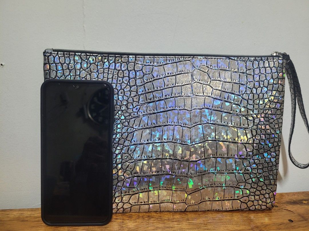 Metallic Holographic Crocodile Pattern Clutch Wristlet Bag (Category: Clutches) located in Pasig City. Submitted by healthnfeshn (Listing ID 1469005838, Image 2). Description: - Style: Silver metallic clutch with embossed crocodile pattern and rainbow iridescent shimmer - Closure: Secure top zipper - Convenience: Attached wrist strap on the right side - Capacity: Roomy interior fits your phone, keys, and cards - Occasion: Ideal for parties, night