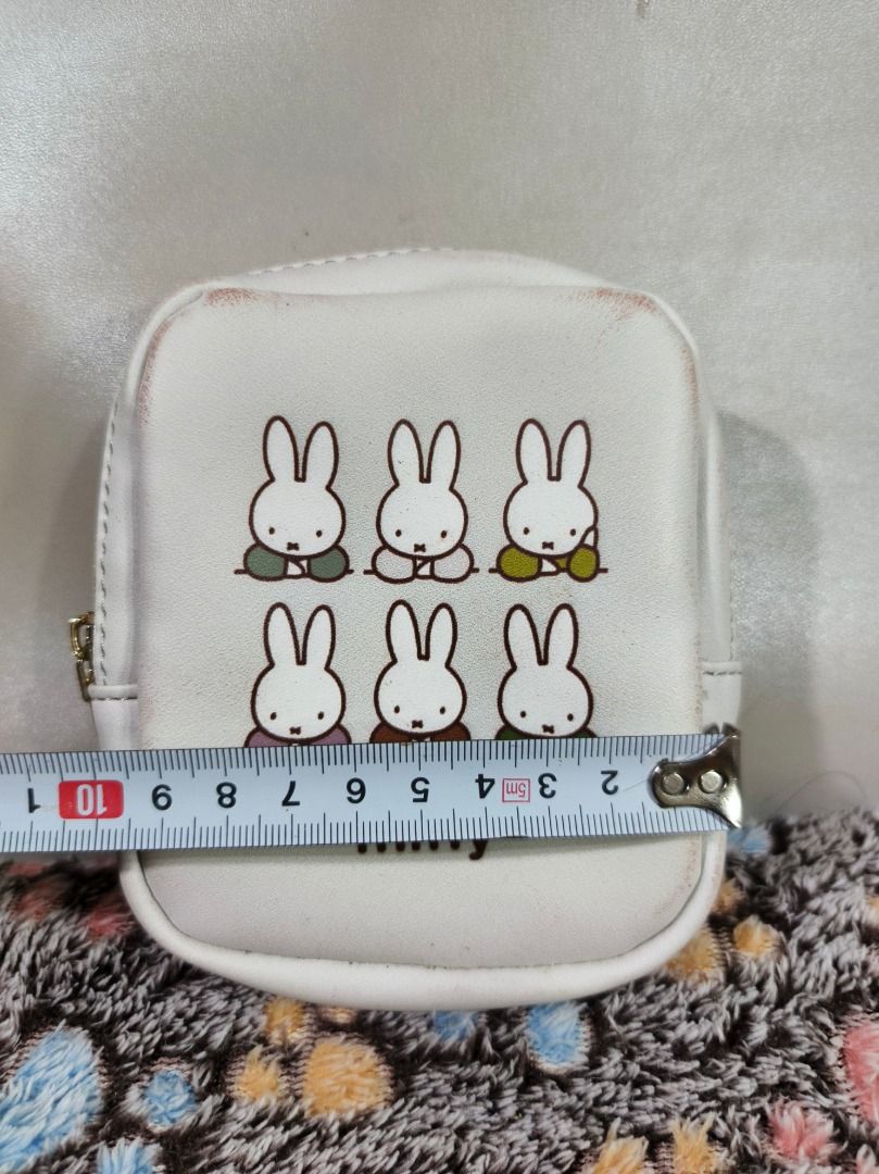 Miffy White Bunny Coin Pouch (Category: Purses & Pouches) located in San Leonardo. Submitted by burgossanleonardo.12345 (Listing ID 1469072754, Image 2). Description: - Authentic Miffy pouch in classic white - Features 6 adorable bunny graphics on the front - Secure gold-tone zipper closure with a chic teardrop pull - Compact size: approx. 9cm (W) x 11cm (H) - Clean interior with smooth-running zipper - Flaw note: Minor discoloration marks near t
