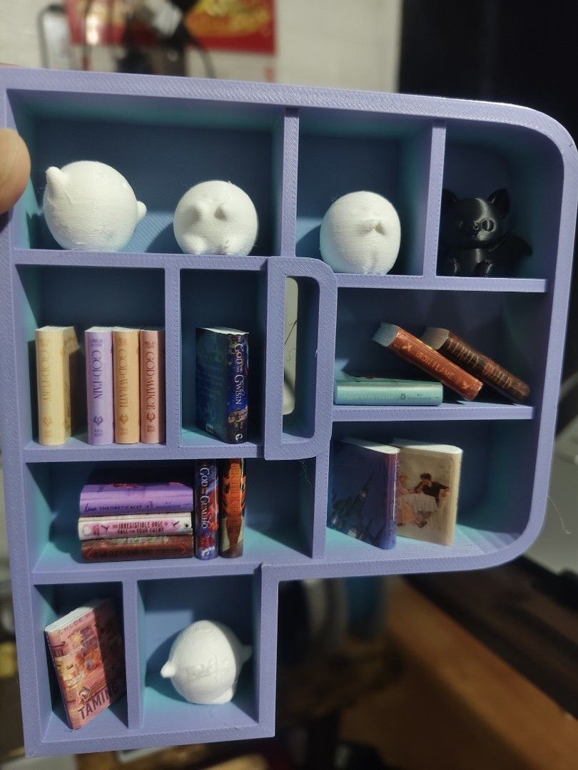 Miniature 3D Printed Book Shelf Display with Tiny Books (Category: Designer & Blind Box Toys) located in Baguio. Submitted by selover1492 (Listing ID 1469102806, Image 3). Description: Handmade 3D printed letter shelf in light purple and teal, filled with tiny books, cute ghosts, and a black cat figure. Perfect desk decor for book lovers and miniature collectors!.