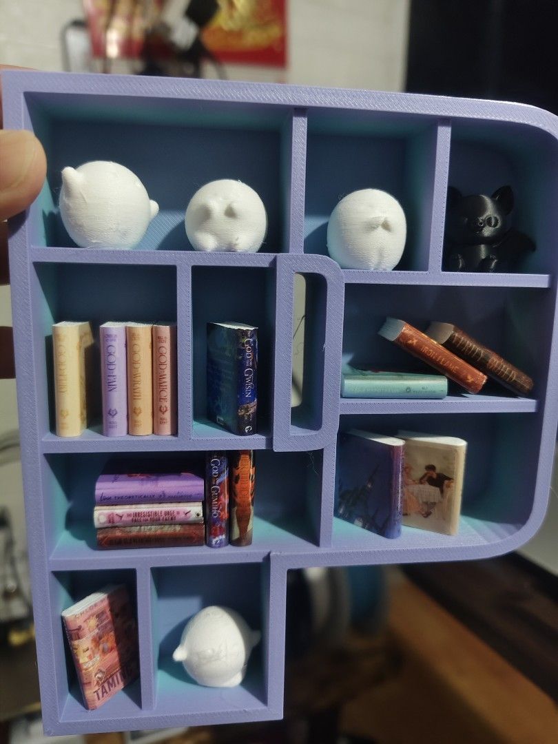 Miniature 3D Printed Book Shelf Display with Tiny Books (Category: Designer & Blind Box Toys) located in Baguio. Submitted by selover1492 (Listing ID 1469102806, Image 1). Description: Handmade 3D printed letter shelf in light purple and teal, filled with tiny books, cute ghosts, and a black cat figure. Perfect desk decor for book lovers and miniature collectors!.