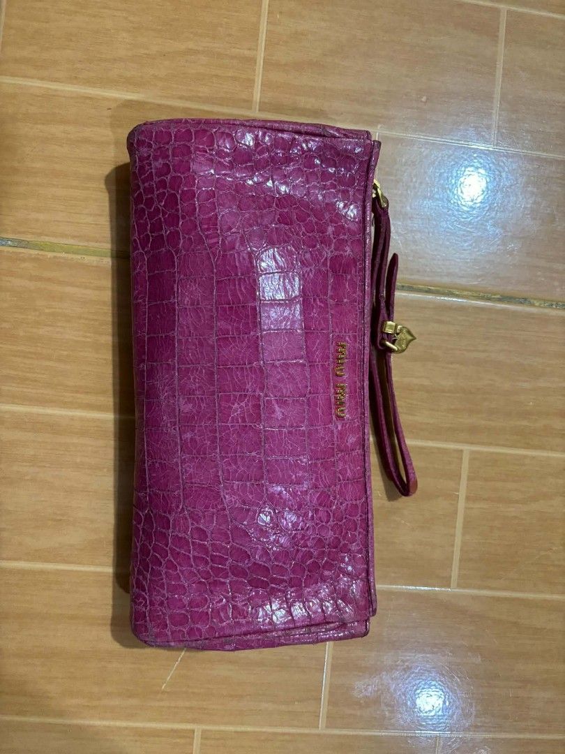 Miu Miu Pink Crocodile Embossed Clutch (Category: Clutches) located in Paranaque City. Submitted by poego (Listing ID 1468954115, Image 3). Description: - Brand: Miu Miu - Color: Bright pink - Material: Embossed crocodile pattern - Hardware: Gold tone with heart-shaped zipper charm - Features: Matching wrist strap and front lettering logo - Size: Compact and handy.