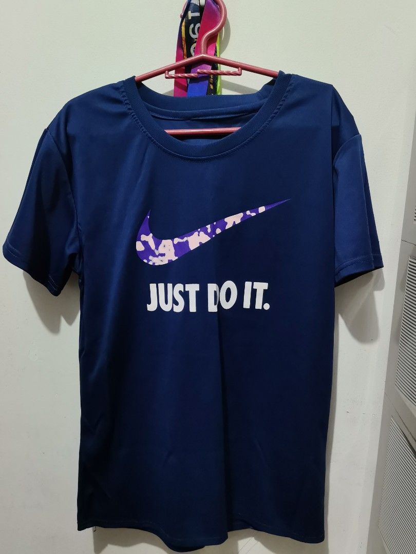 Nike Blue Just Do It T-Shirt (Category: Tshirts & Polo Shirts ) located in Valenzuela. Submitted by paaaatt (Listing ID 1469017069, Image 1). Description: Dark blue Nike t-shirt with short sleeves and a crew neck. Front graphic features a purple and pink camo swoosh above white text saying JUST DO IT. Back is plain solid dark blue. Soft athletic fabric..