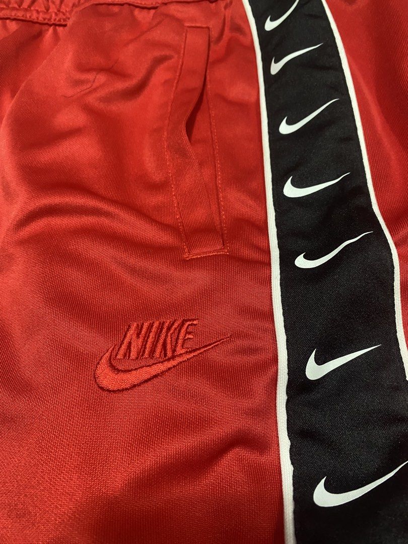 Nike Red Track Pants Repeat Tape Size M (Category: Joggers) located in Manila. Submitted by japhetcond32104 (Listing ID 1469111046, Image 2). Description: - Brand: Nike - Color: Bright red with black side taping - Features: Multiple white swoosh logos down each leg, embroidered red Nike logo near pocket, drawstring elastic waist, and zip ankles - Size: Medium - Material: 100% polyester (Made in Vietnam) - Condition: Clean inside and out.